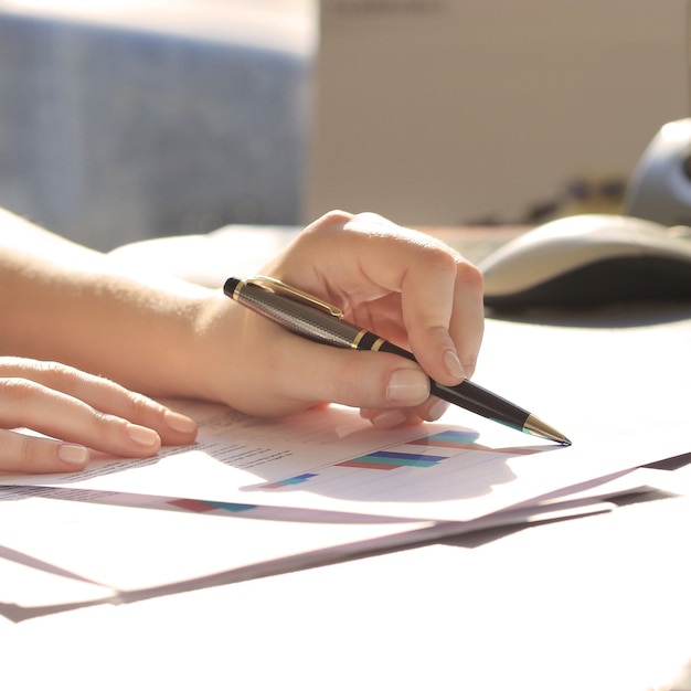 A close-up shot of a person's hand holding a pen and signing mortgage documents, with a calculator and financial reports subtly blurred in the background.
